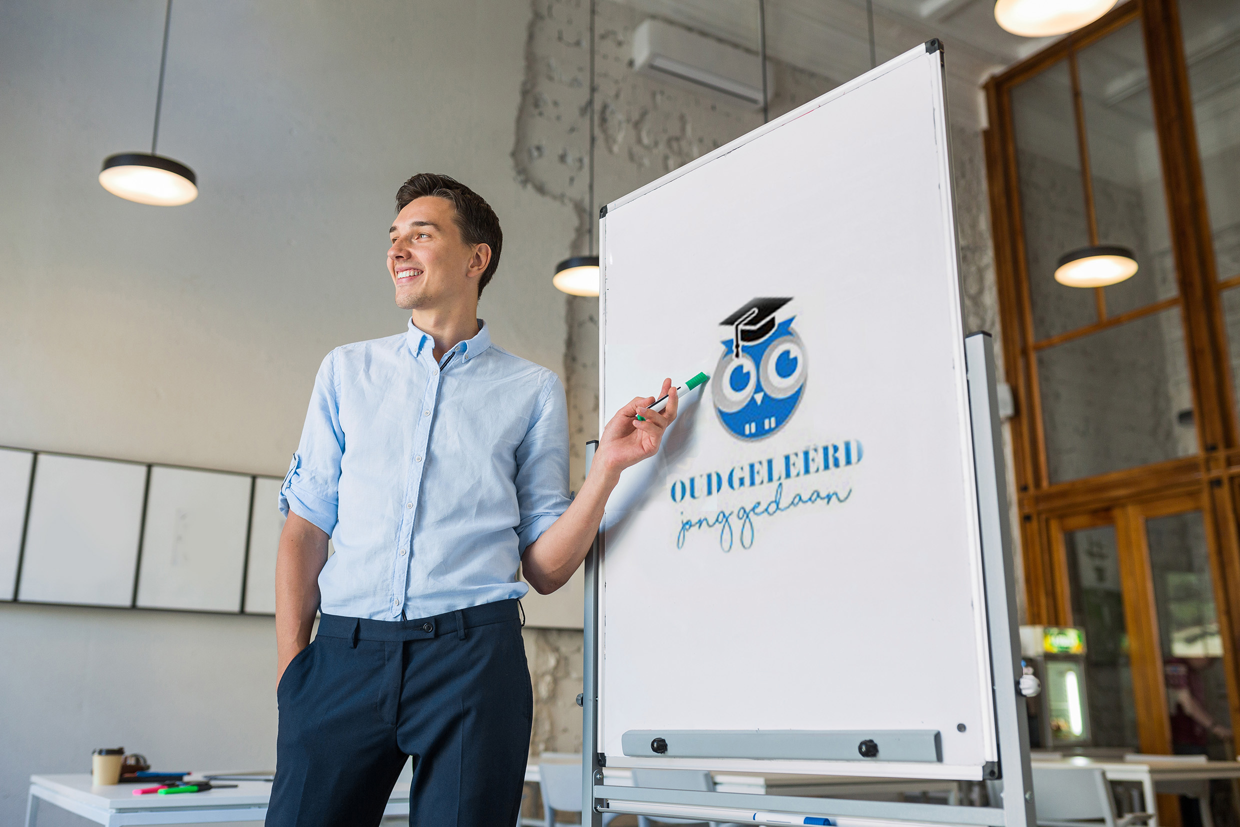 attractive young handsome smiling man standing at empty white board with marker, leadership business training in open space office, successful modern youth, online education